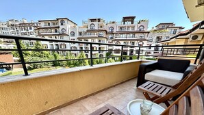 A balcony with a wooden table and a cushioned chair, overlooking a row of buildings with balconies. - Menada Paradise Dreams Apartments (Sveti Vlas)