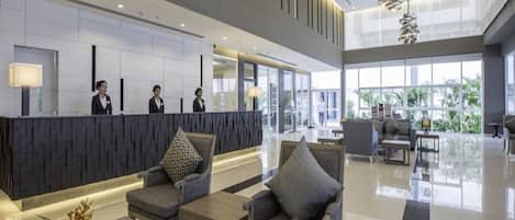Un lobby moderno de hotel con mostrador de recepción, zona de estar y ventanas amplias.
