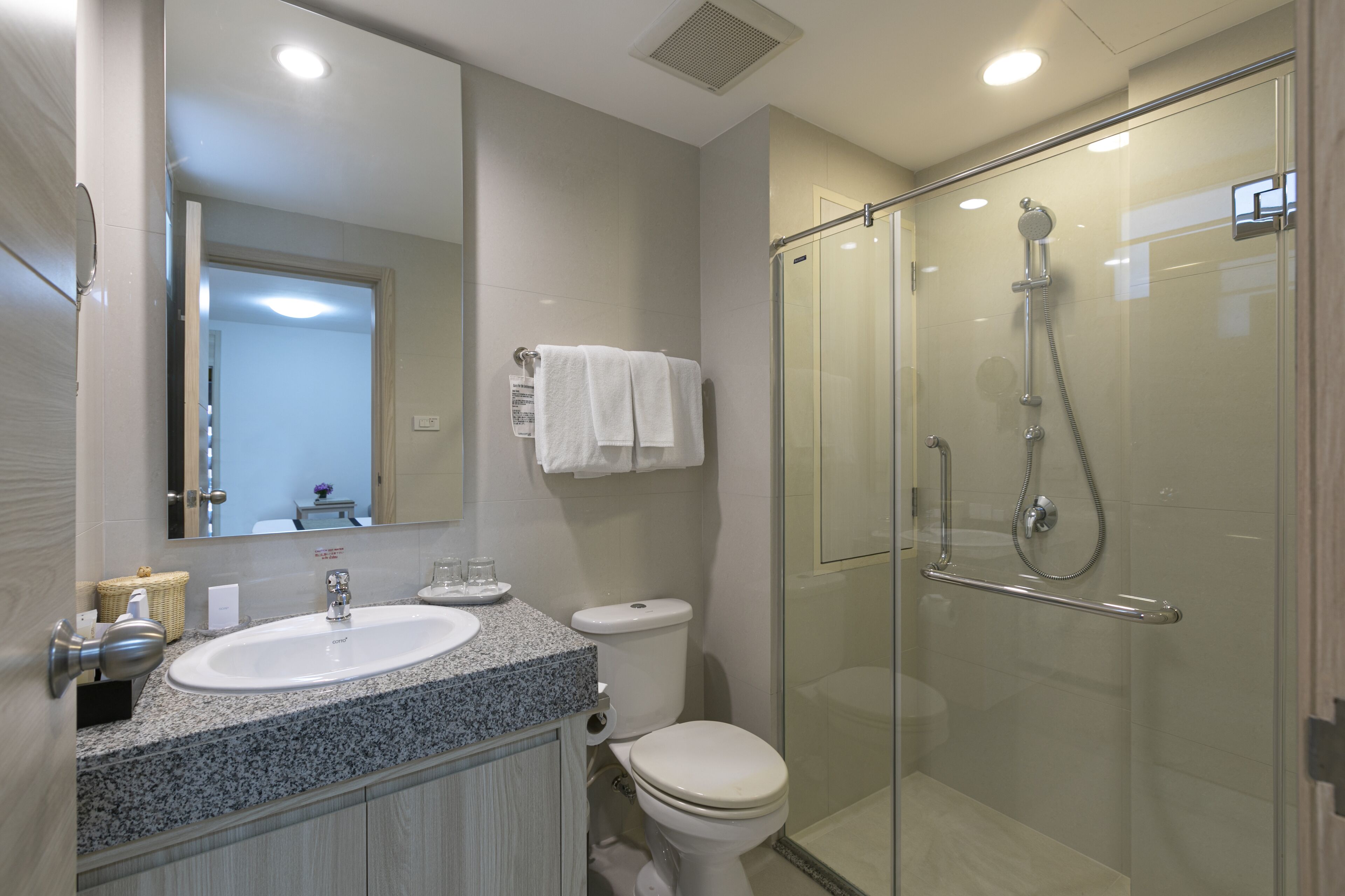 A modern bathroom with a granite countertop sink, a toilet, and a glass-enclosed shower.