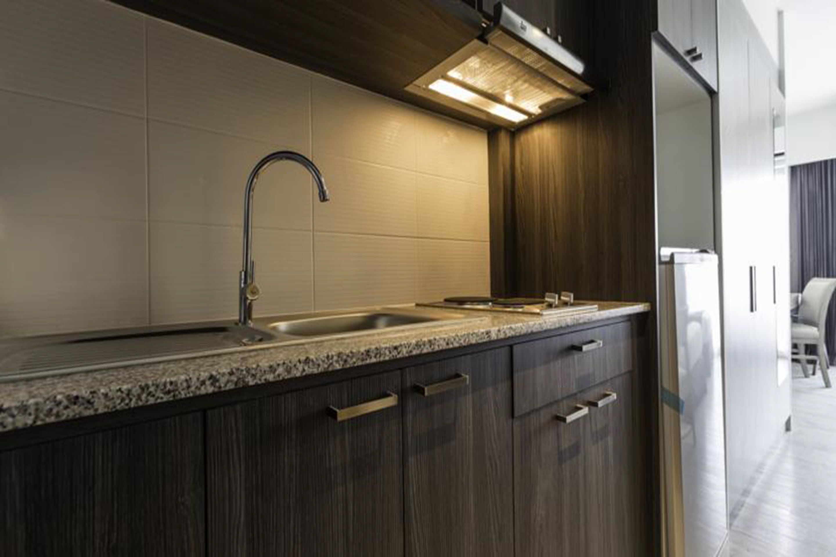A modern kitchen with dark wood cabinets, a granite countertop, a stainless steel sink, and a built-in oven.