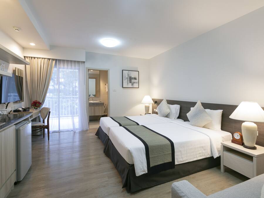 Quarto de hotel com cama, mesas de cabeceira, escrivaninha e cozinha compacta.