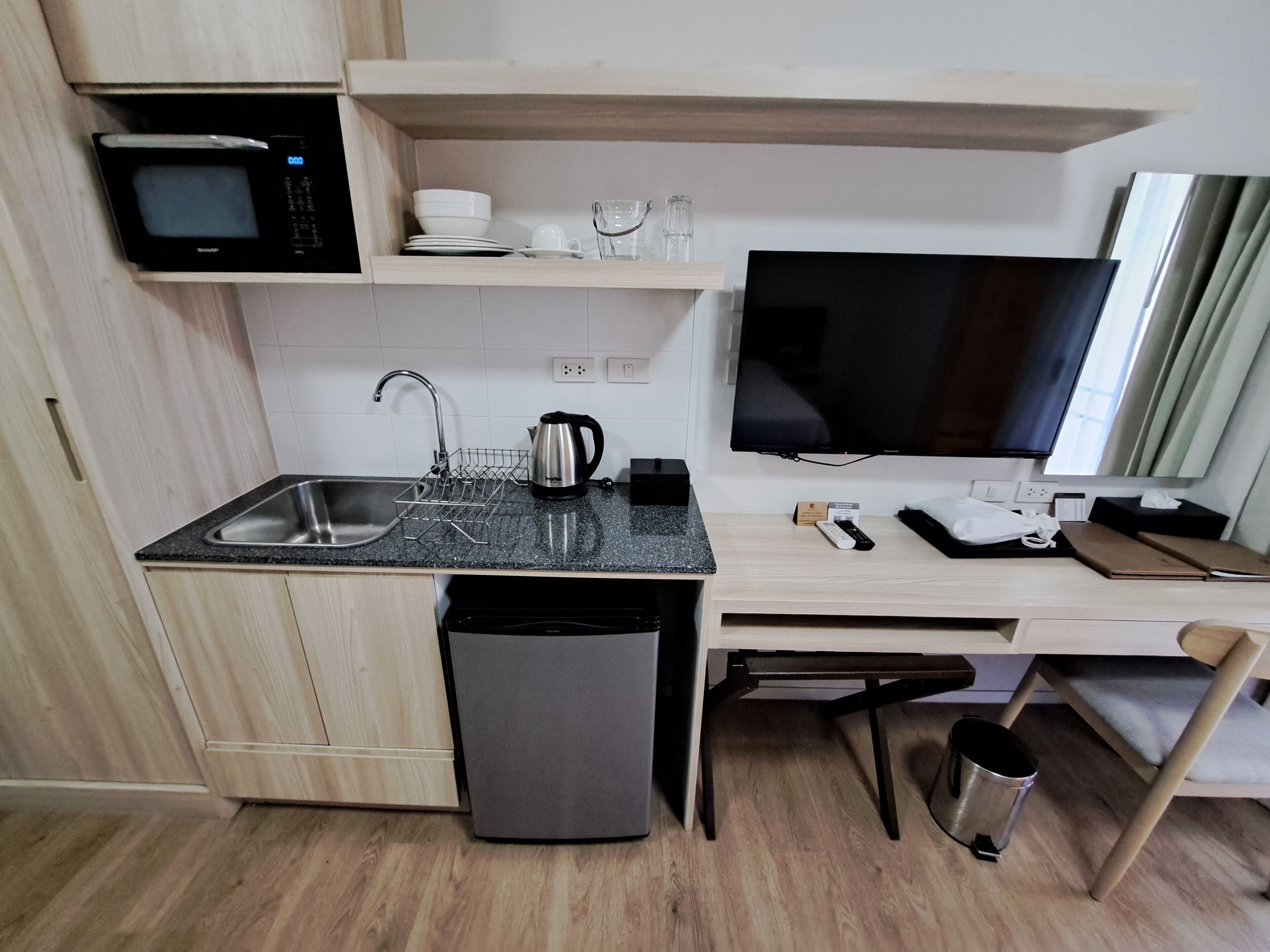 A compact kitchen with a microwave, sink, kettle, and a flat-screen TV.
