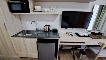 A compact kitchen with a microwave, sink, kettle, and a flat-screen TV.
