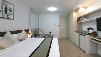 A modern hotel room with a bed, bedside table, lamp, and a view of the kitchen area.