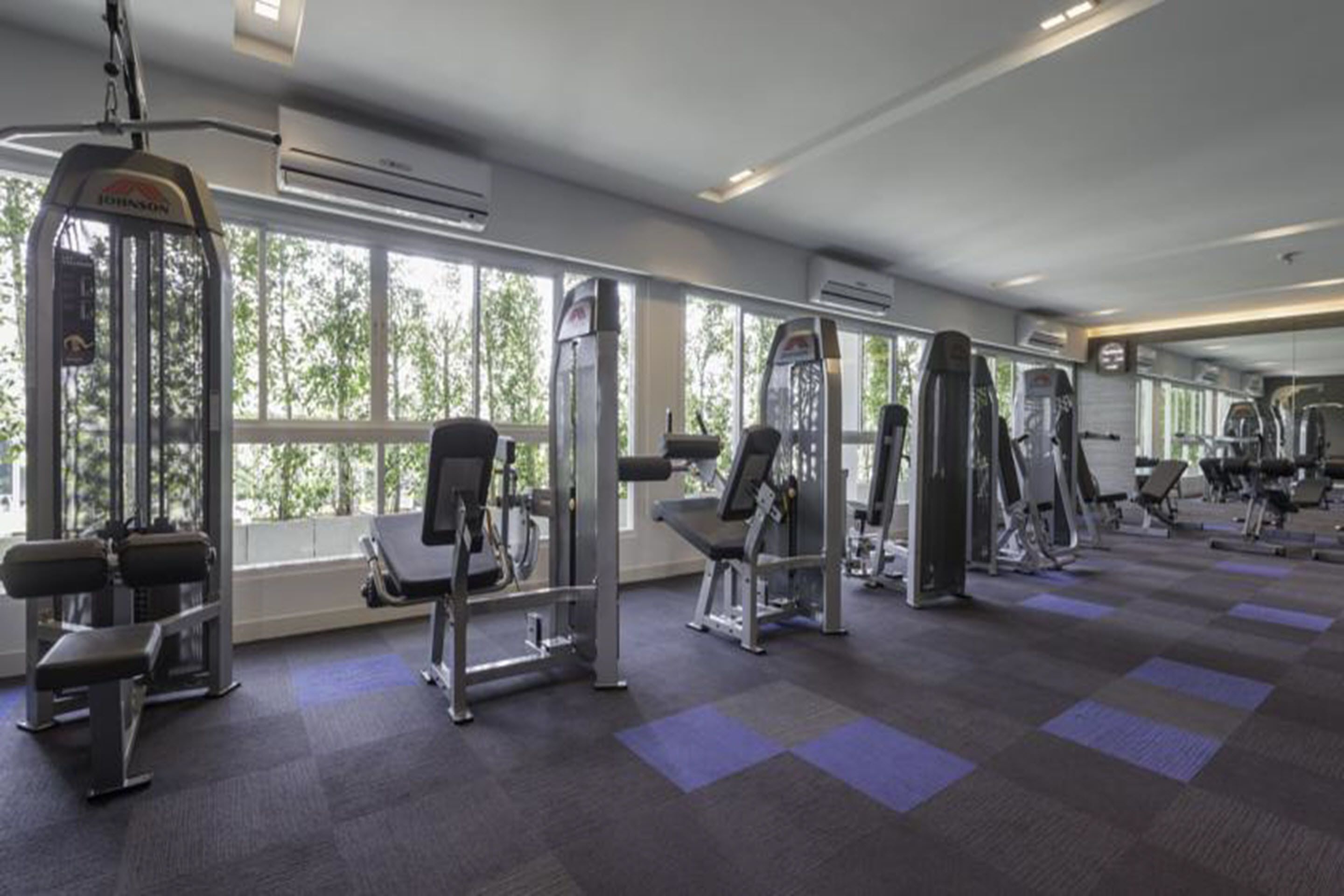 Une salle de sport équipée de divers appareils d’exercice, dotée de grandes fenêtres et d’un sol recouvert de moquette.