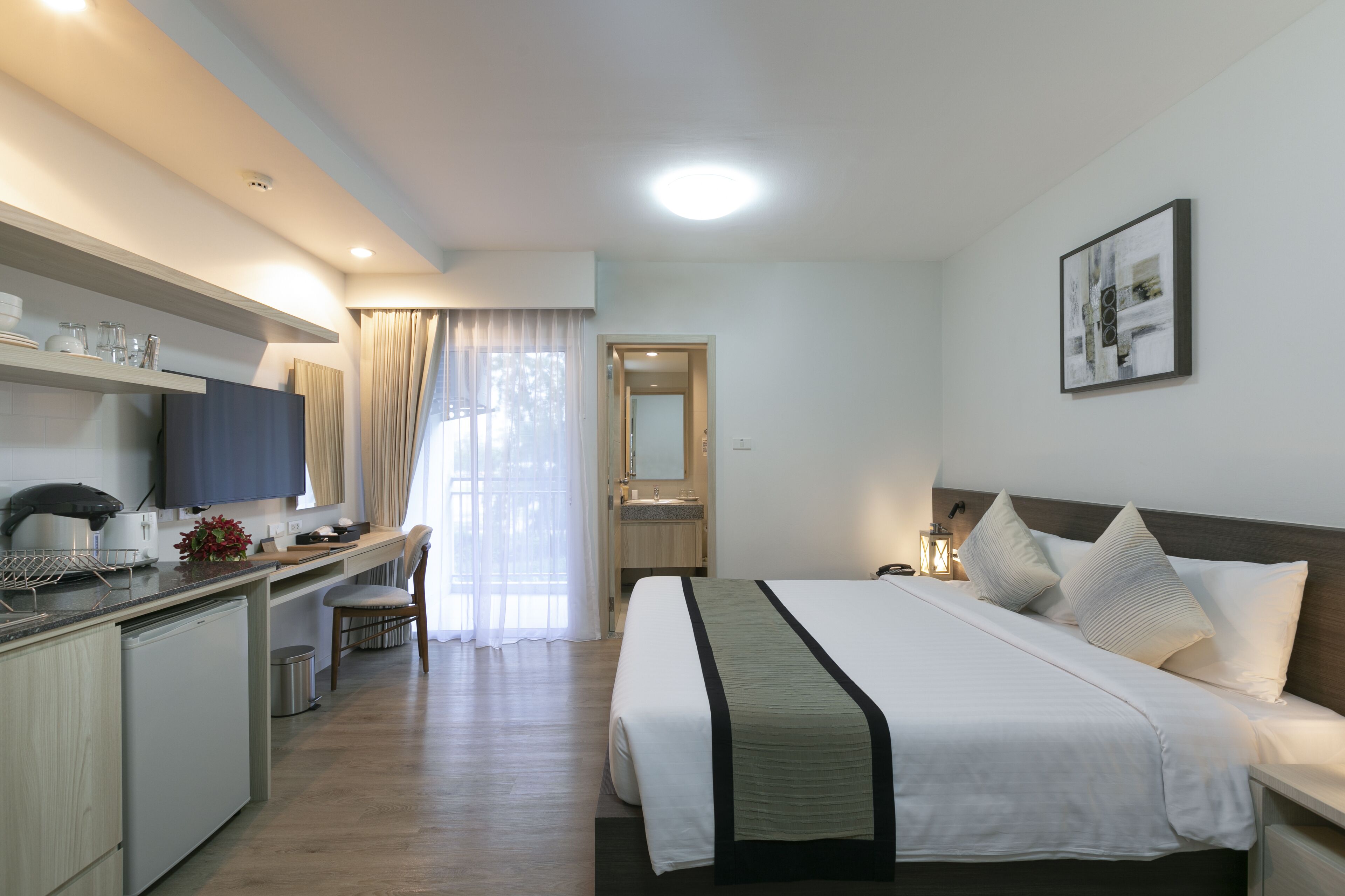 A modern hotel room with a bed, bedside table, and a desk with a chair.