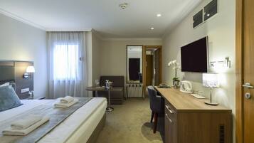 A hotel room with a bed, bedside table, desk, chair, and a television.