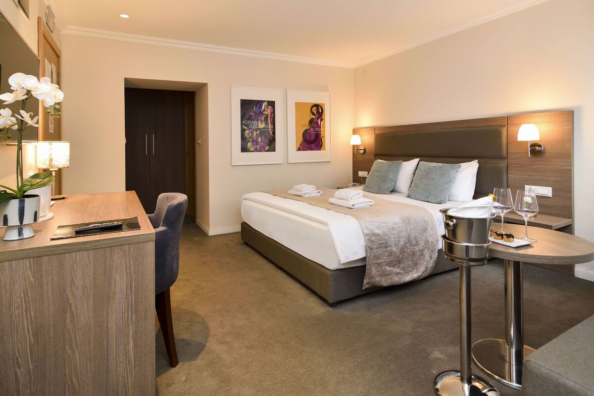 A modern hotel room with a bed, bedside table, lamp, and artwork on the wall.