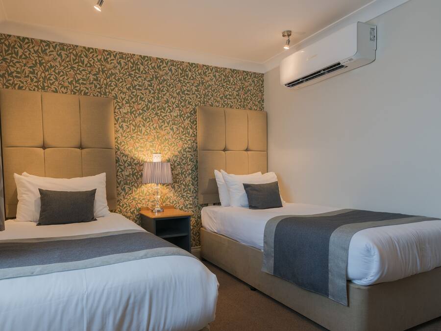 Habitación de hotel con dos camas, una mesita de noche con lámpara y aire acondicionado instalado en la pared.