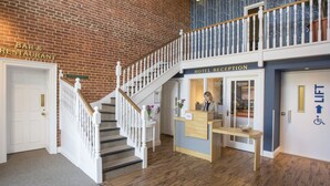 A hotel reception area with a brick wall, a staircase, and a sign for the bar and restaurant.