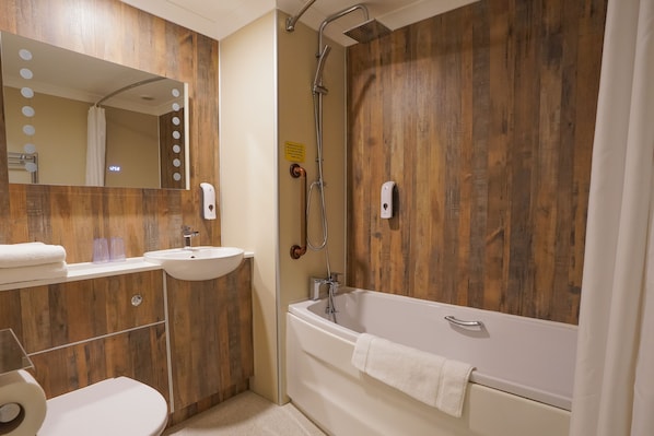 A bathroom with a wooden wall, a bathtub, a shower, a sink, and a mirror with lights. - Old Hall Hotel (Great Yarmouth)