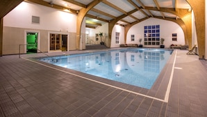 An indoor swimming pool with a tiled floor, wooden beams, and a green exit door.