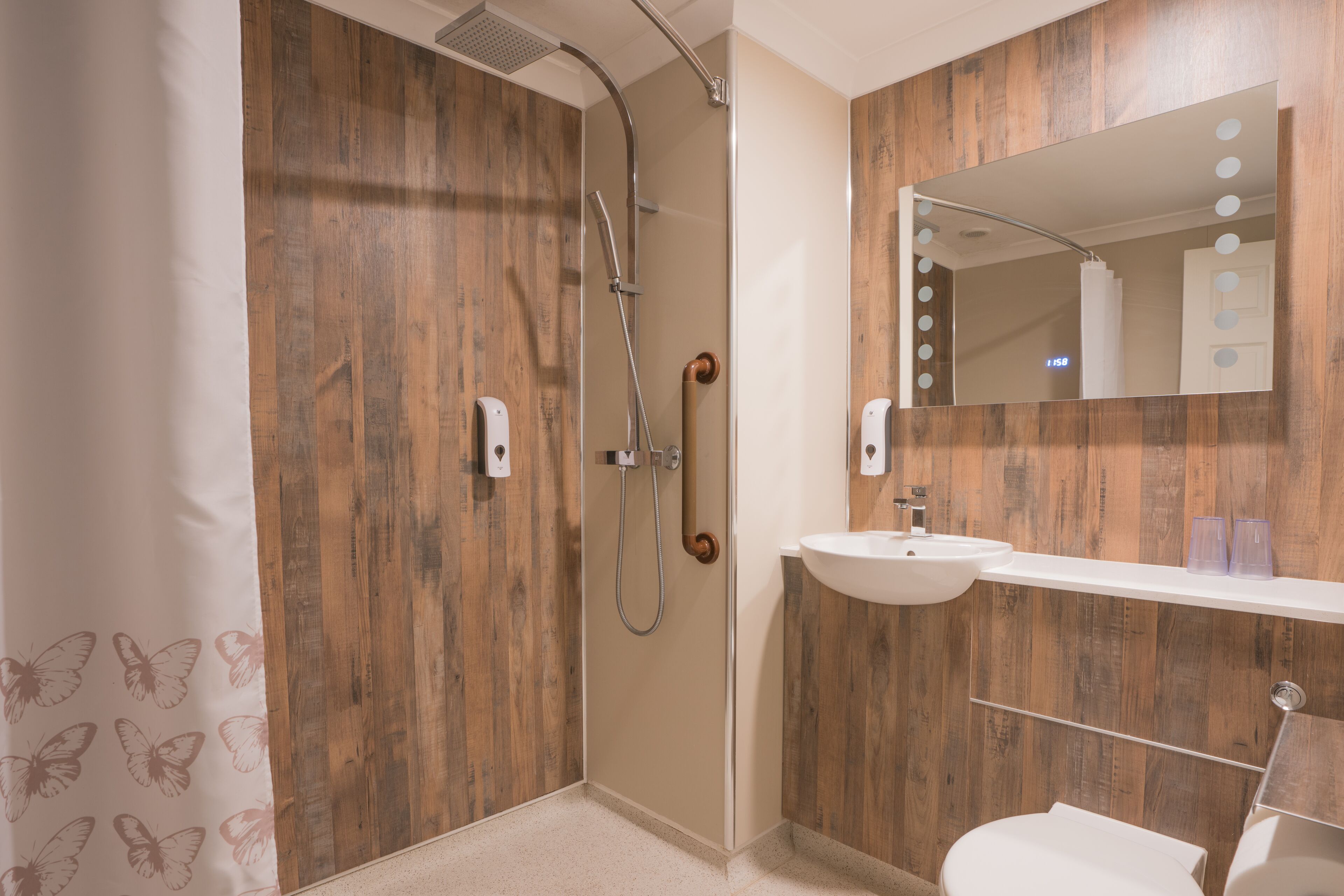 A modern bathroom with a wooden wall, a shower, a sink, and a mirror with lights.