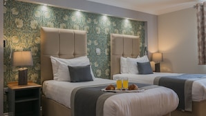 A hotel room with two beds, a nightstand, and a tray with croissants and orange juice.