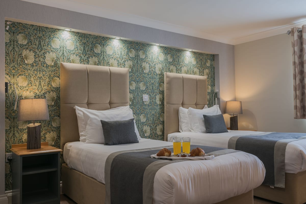 Ein Hotelzimmer mit zwei Betten, einem Nachttisch und einem Tablett mit Croissants und Orangensaft.