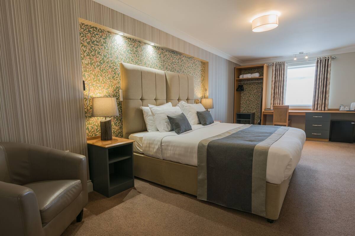 Ein Hotelzimmer mit einem großen Bett, einem Nachttisch, einem Sessel, einem Schreibtisch und einem Kleiderschrank.