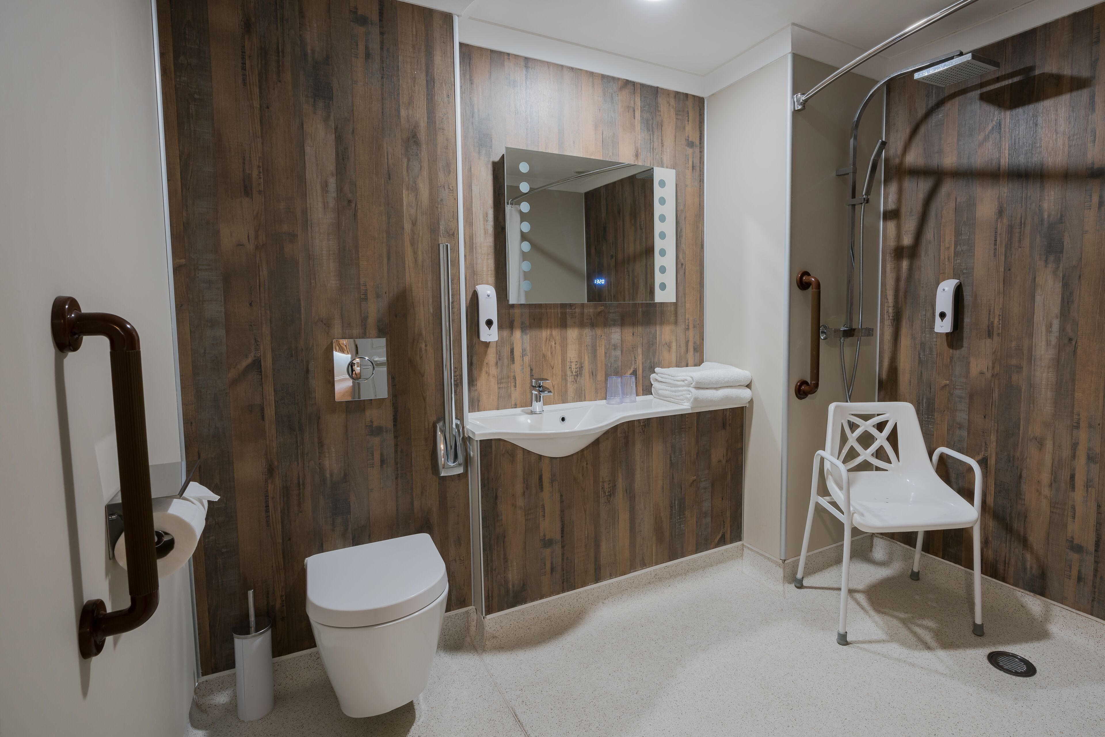A modern bathroom with a wooden wall, a white sink, a toilet, a shower, and a white chair.