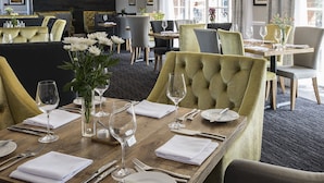 A restaurant with tables set for dining, featuring a mix of upholstered and cushioned chairs, and a view of the dining area through a glass partition.