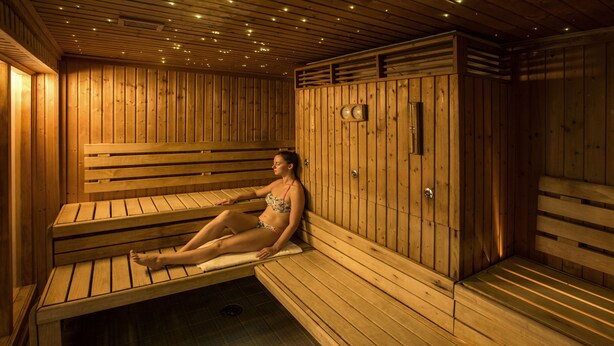 A sauna room with wooden benches and a bench seat, a wooden wall with a clock, and a bench with a towel.