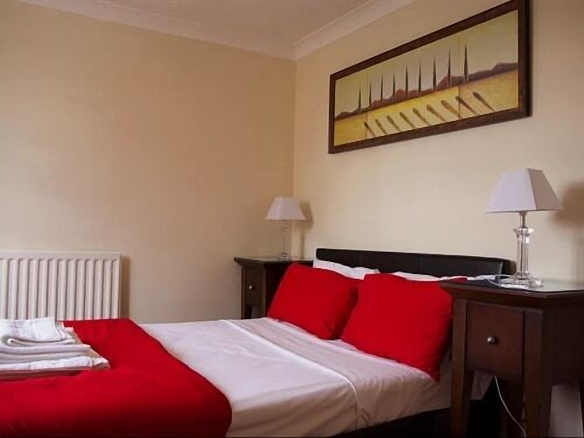 Une chambre d’hôtel avec un lit, deux tables de chevet avec des lampes, un radiateur et un tableau au mur.