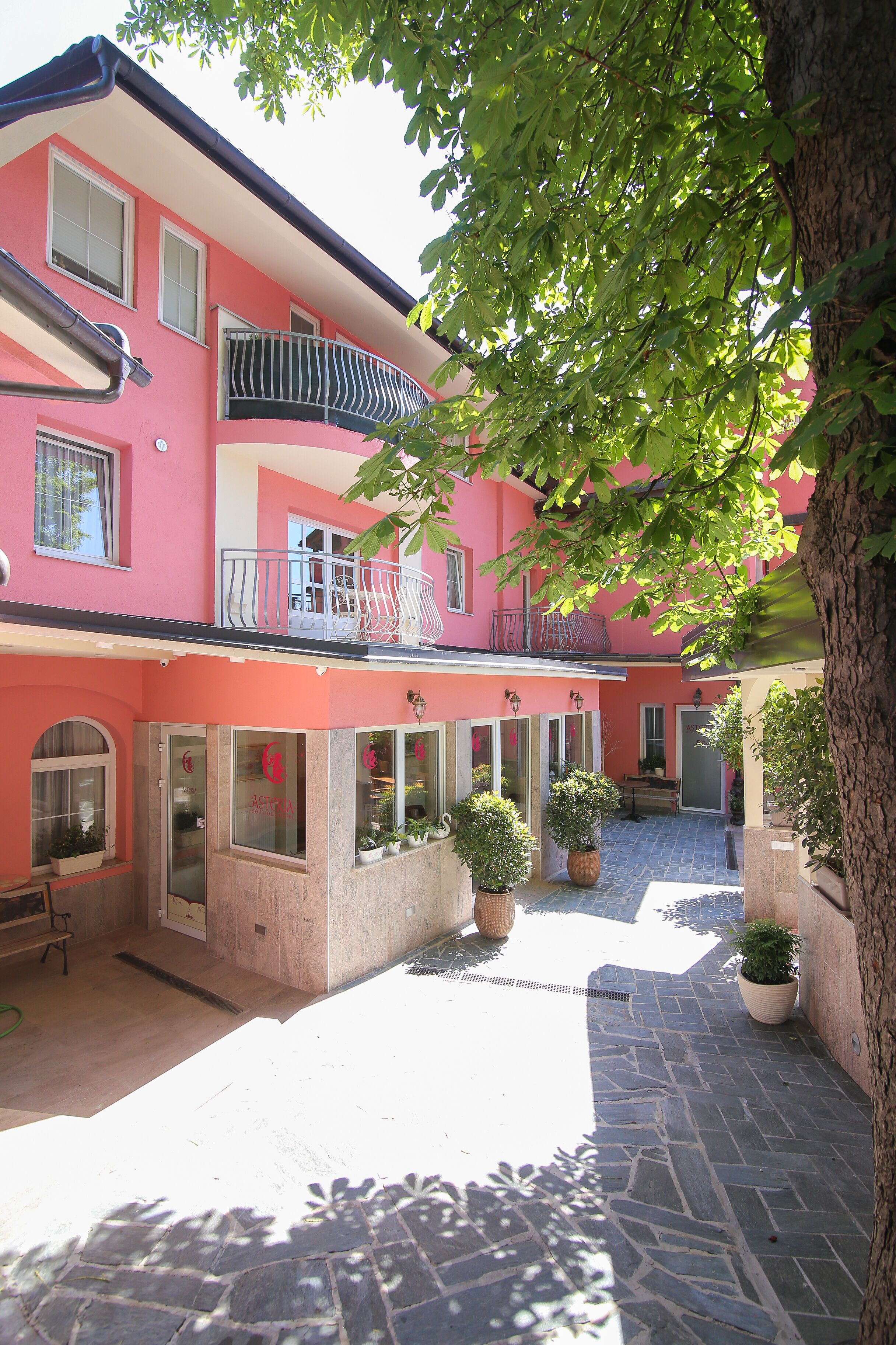 A pink building with a balcony, potted plants, and a stone courtyard.