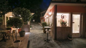 A hotel entrance with a sign reading "HASTERIA Boutique Hotel," a potted plant, and a table with chairs outside.