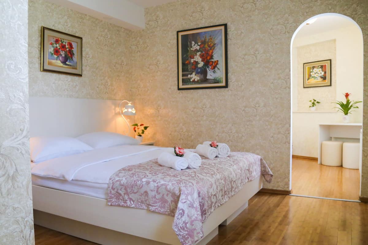 A neatly made bed with white linens and a floral-patterned bedspread, a bedside lamp, and two framed floral paintings on the wall.