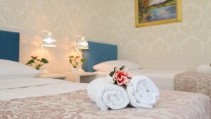 Een netjes opgemaakt bed met opgerolde witte handdoeken en een decoratieve bloem, een nachtkastje met een lamp, en een schilderij aan de muur.