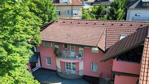 Een meerlaags roze gebouw met een betegeld dak, een balkon en een binnenplaats met buiten zitplaatsen.