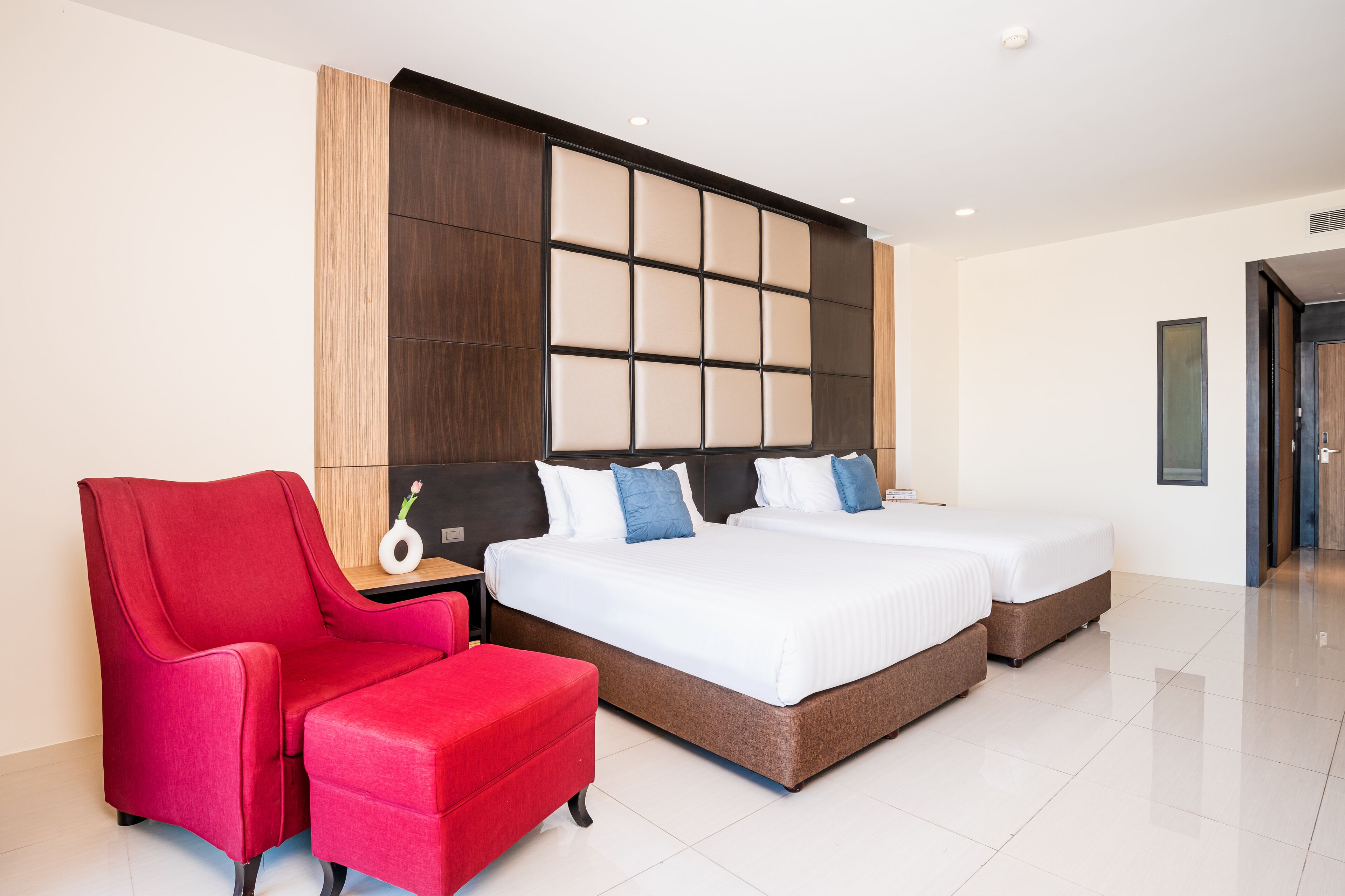 A hotel room with a large bed, two bedside tables, a red armchair, and a wooden panel wall.