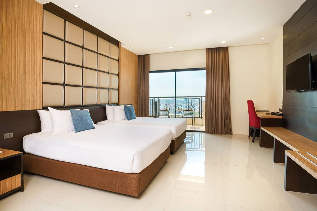 A modern hotel room with a large bed, a desk, a TV, and a balcony with a view.