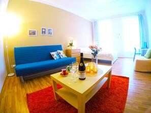 A modern living room with a blue sofa, a wooden coffee table with a bottle of wine, glasses, and candles, and a red rug. - Lidicka Apartments (Prague)