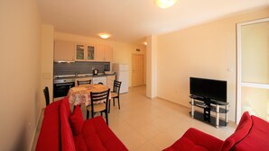 Ein kompakter Wohnraum mit Küchenzeile, einer Essecke mit Tisch und Stühlen sowie einer Sitzecke mit roten Sofas.