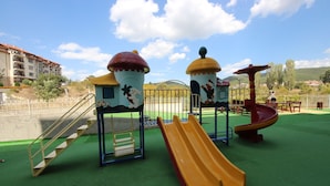 Ein Spielplatz mit Rutschen und Treppen, umzäunt und mit Gebäuden im Hintergrund.