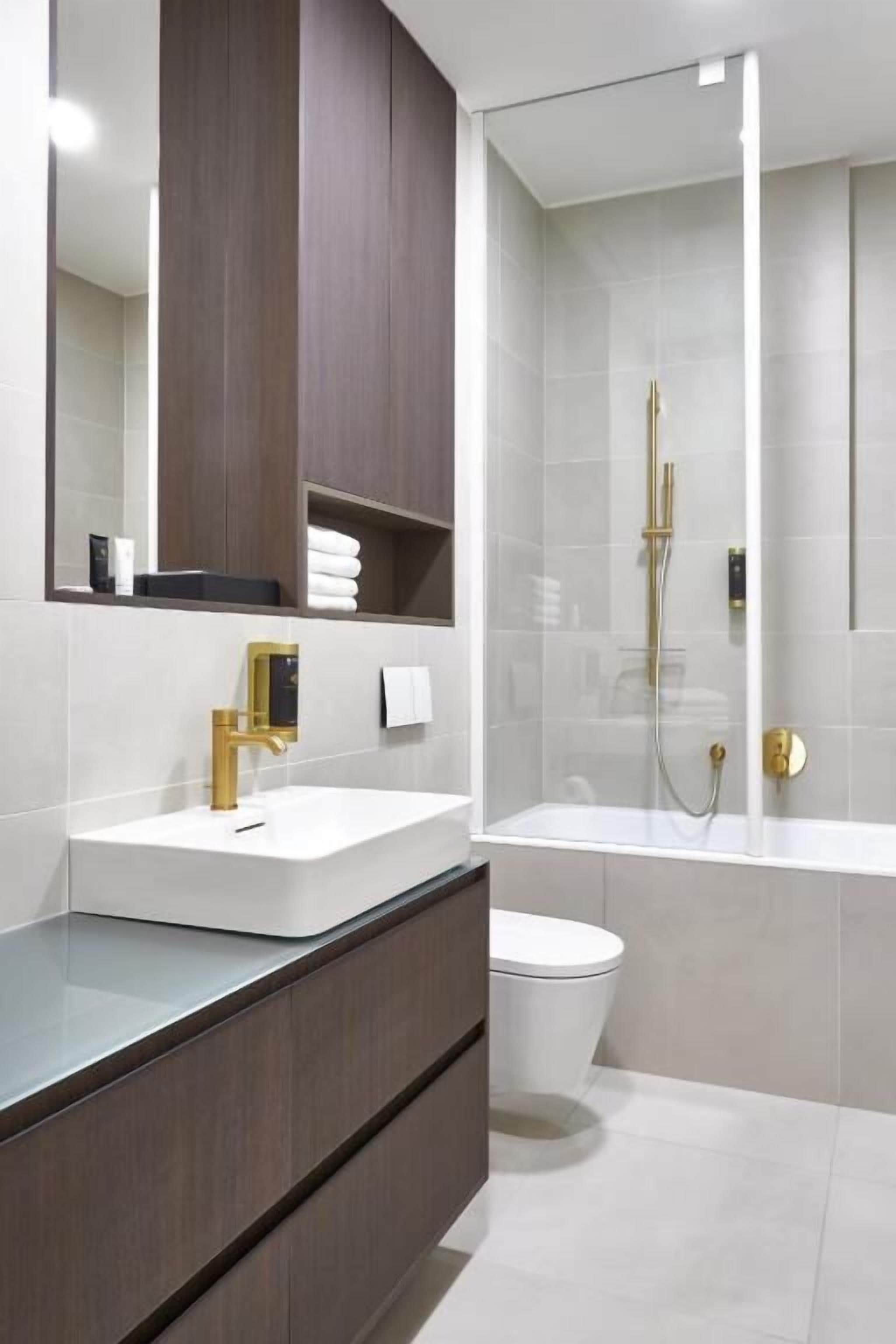 A modern bathroom with a white sink, gold faucet, and a glass-enclosed shower.