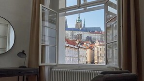 A room with a large window offering a view of historic buildings and a prominent tower. - Three Golden Crowns Apartments (Prague)