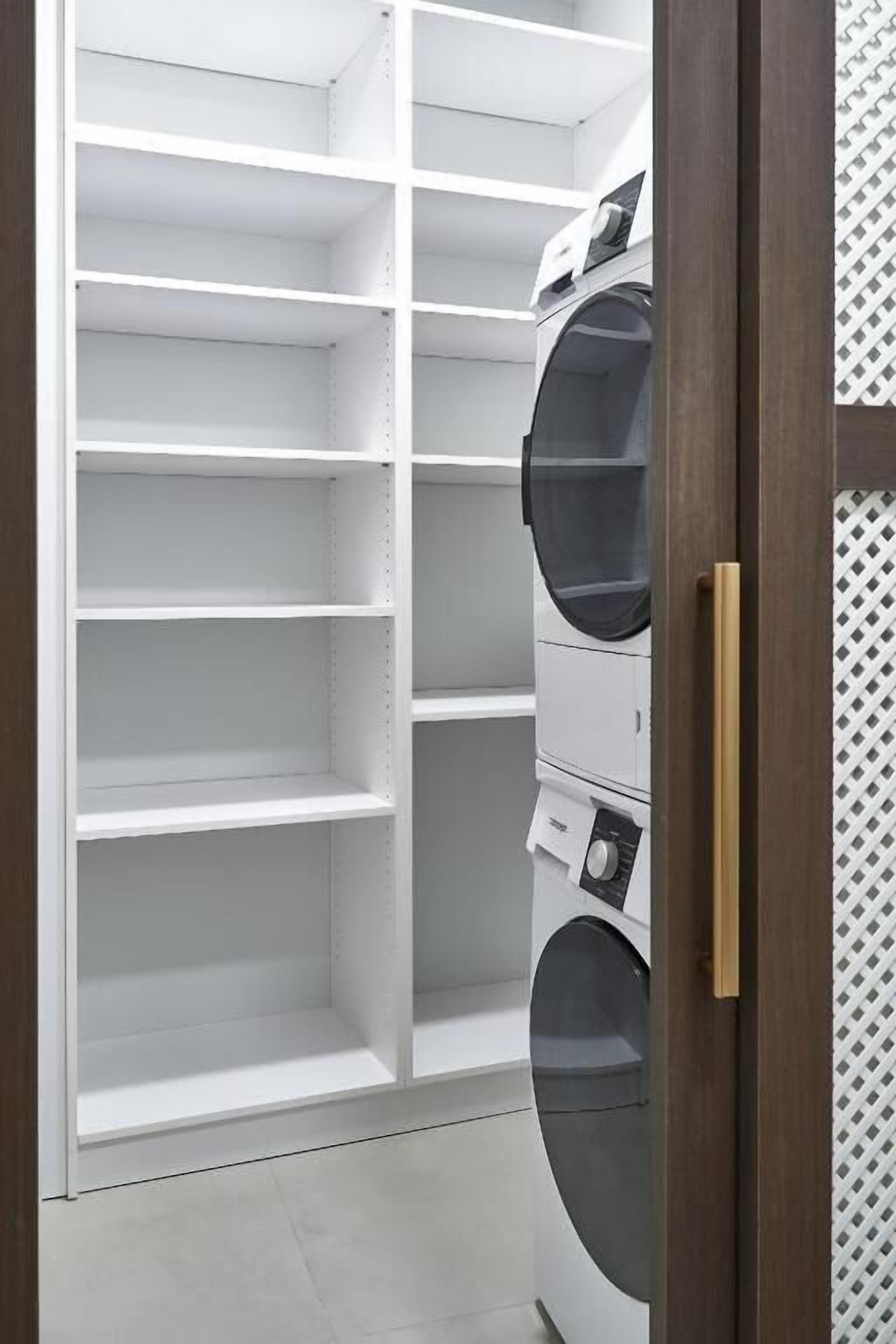 A laundry room with a white shelving unit and a stacked washer and dryer.