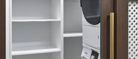 A laundry room with a white shelving unit and a stacked washer and dryer.