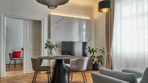 A modern living room with a round black table, grey chairs, a large TV, and a potted plant. - Three Golden Crowns Apartments (Prague)