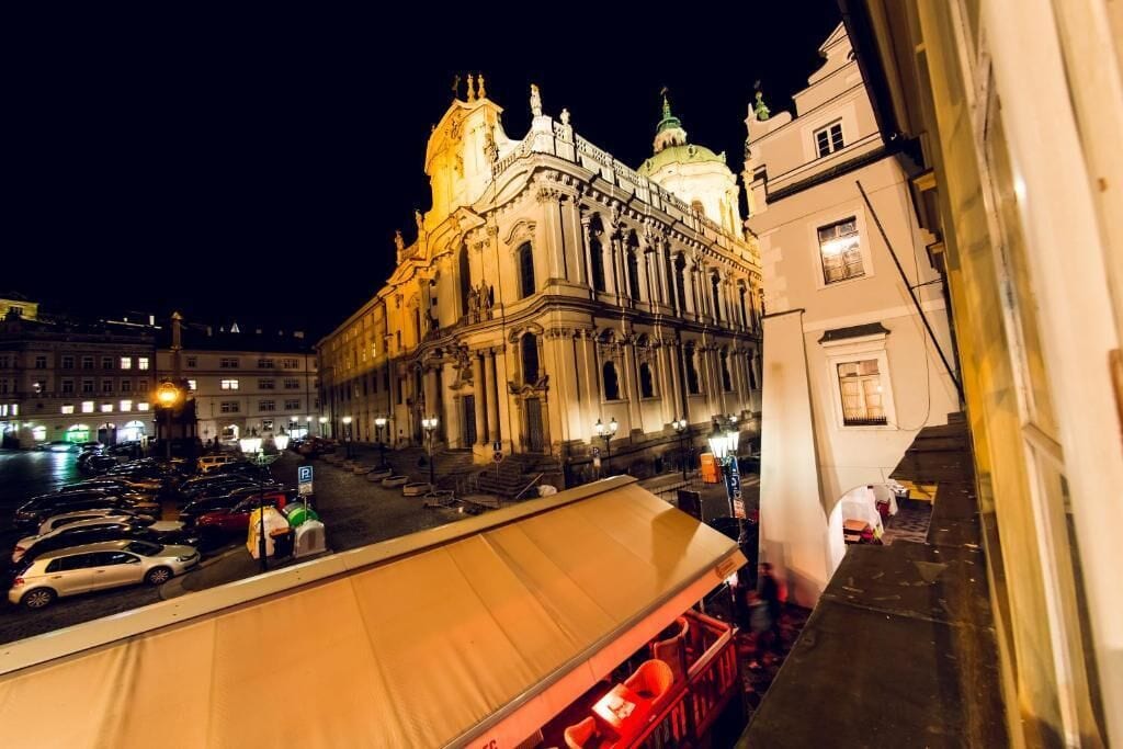 A nighttime view of a historic building with classical architecture, a covered outdoor seating area, and a parking lot.