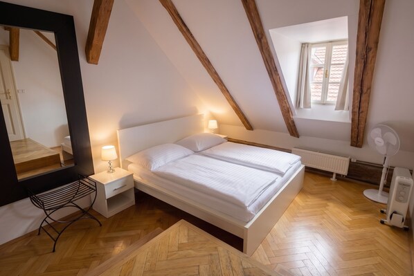 A bedroom with a bed, bedside tables, a mirror, a window, and a radiator. - Three Golden Crowns Apartments (Prague)
