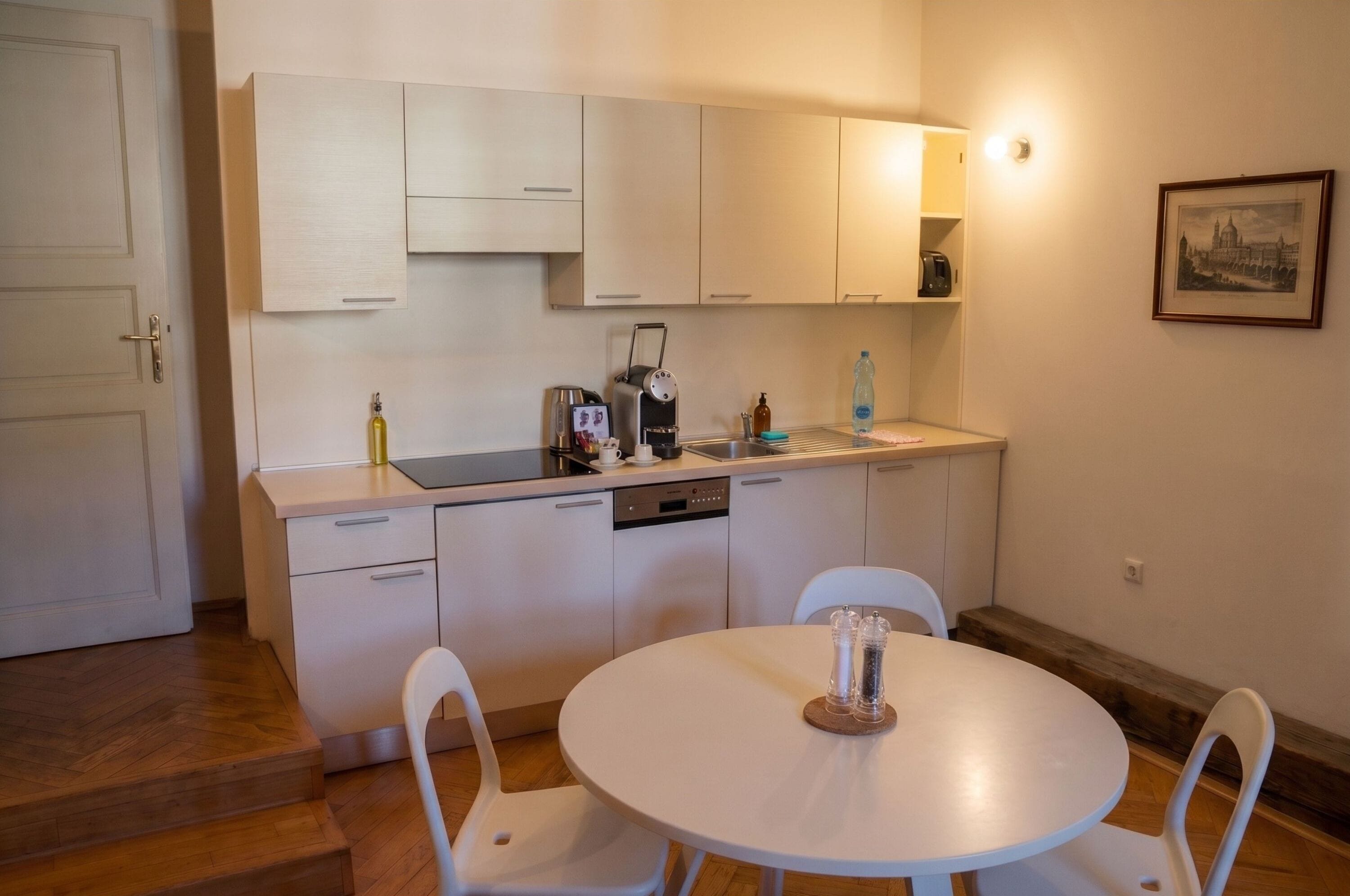 Una cocina compacta con armarios blancos, una cafetera, un lavamanos y una mesa de comedor con sillas.
