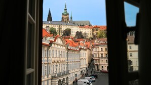 A view through a window of a historic building with a prominent tower and a street with parked cars. - Three Golden Crowns Apartments (Prague)
