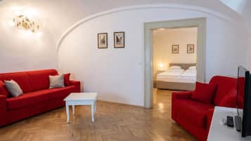 A room with a red sofa, a white table, a TV, and a bed in the background.