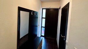 Un pasillo estrecho con una puerta oscura al final, un interruptor de luz arriba y una ventana con vidrio esmerilado.