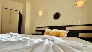 Una cama bien hecha con sábanas blancas, cabecera con líneas horizontales y un espejo redondo sujeto a la pared.