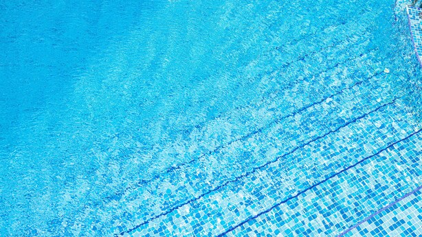 Primer plano del borde de una piscina con agua cristalina y diseños de baldosas visibles.