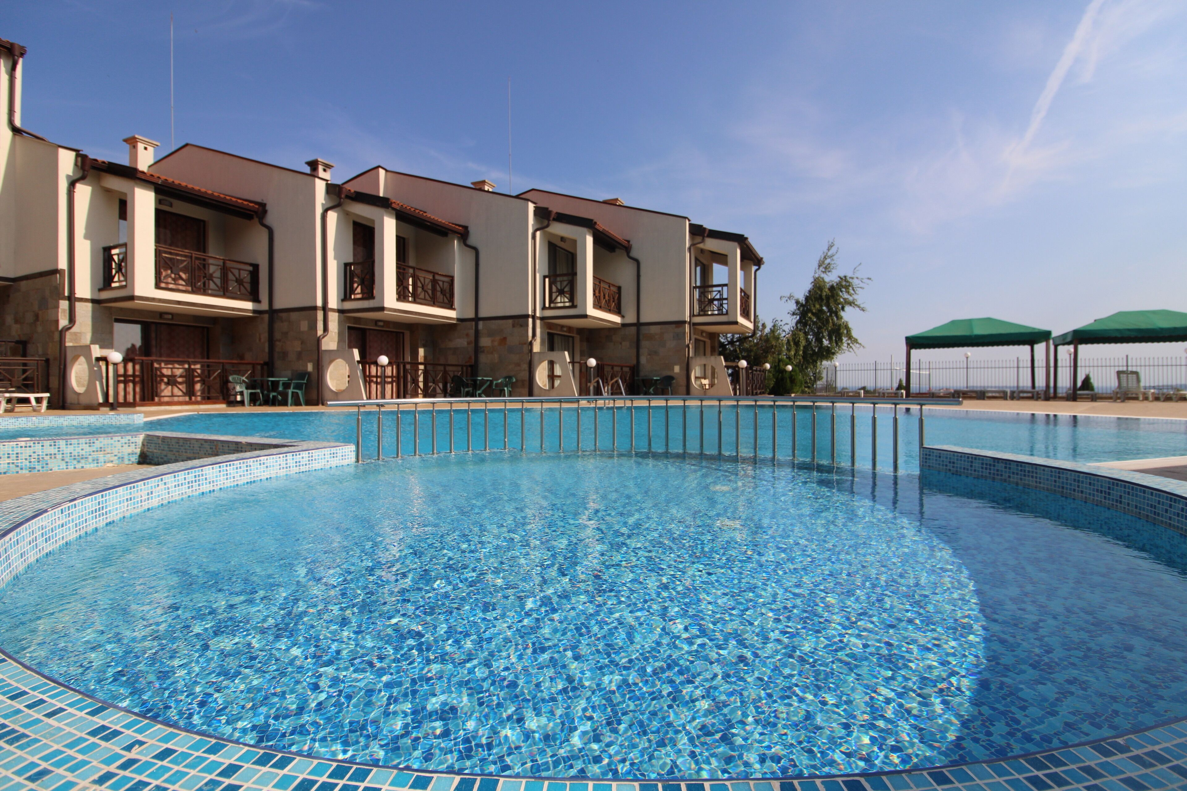 A swimming pool with a tiled edge, surrounded by a building with balconies and outdoor seating.