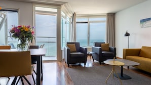 A modern living room with a view of the sea, a dining area with a vase of flowers, and a cozy seating arrangement.