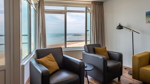A room with two leather armchairs, a floor lamp, and a large window overlooking a beach.